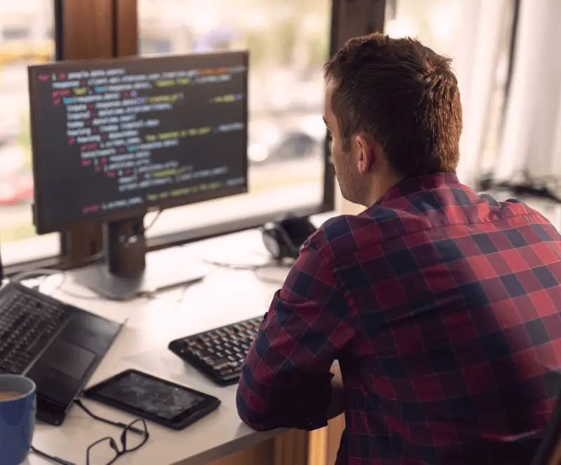 Image of a man working at his desk, looking at code on his computer