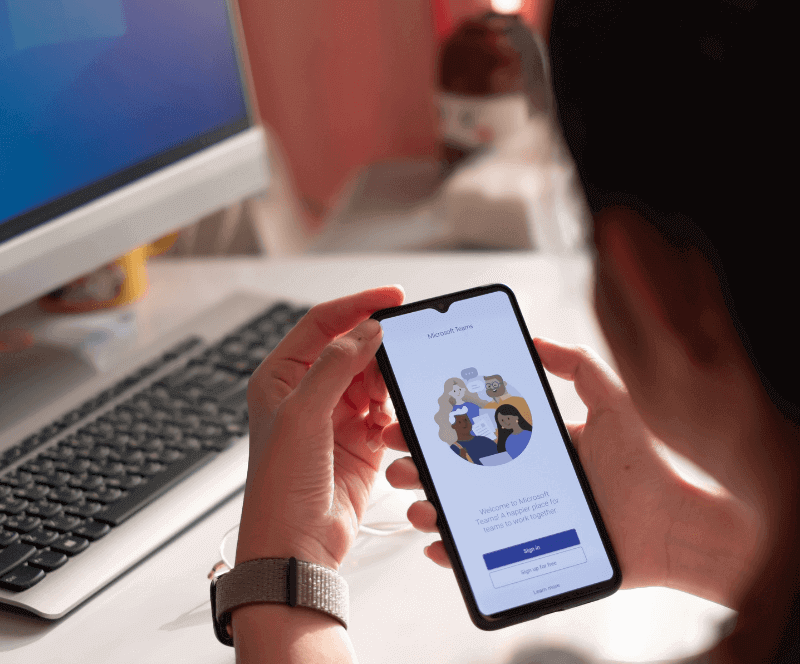 Image of a man sitting at his desk using Microsoft Teams on his phone